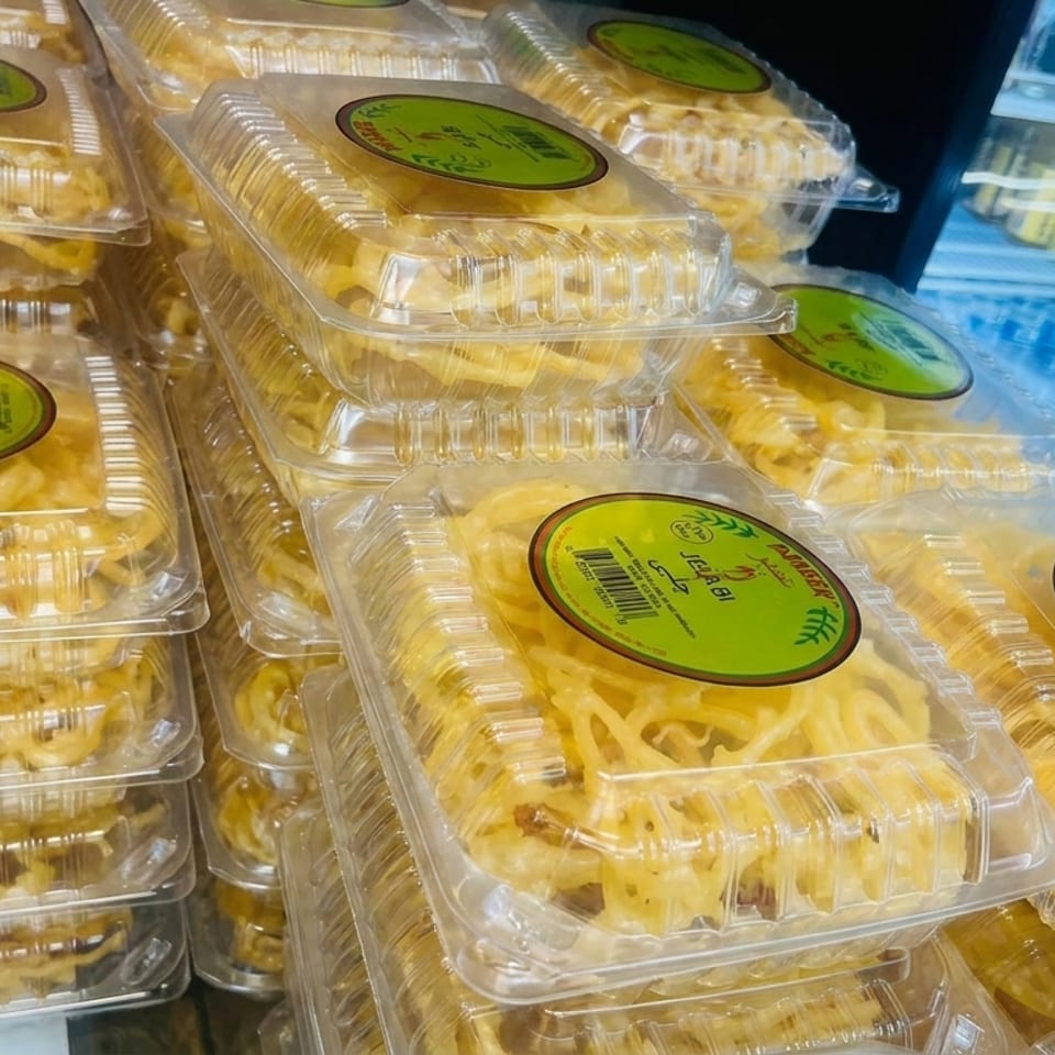 Stacks of packaged noodles in clear containers displayed beside a refrigerated beverage case.